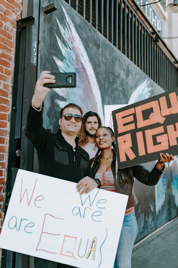 who-we-are Group of people holding equality signs taking a selfie during a protest.