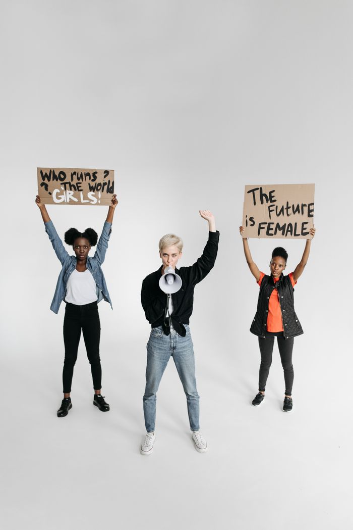 A diverse group of women holding protest signs and a megaphone advocating for gender equality.