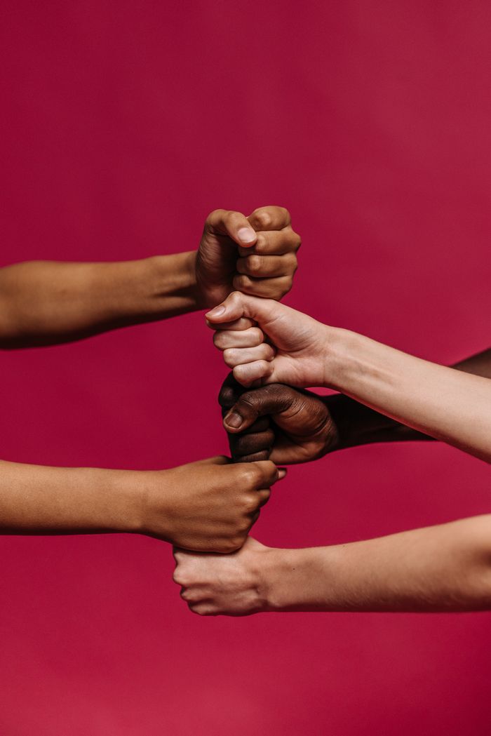services-03 Close-up of diverse hands forming fists, symbolizing unity and teamwork on a vivid pink background.